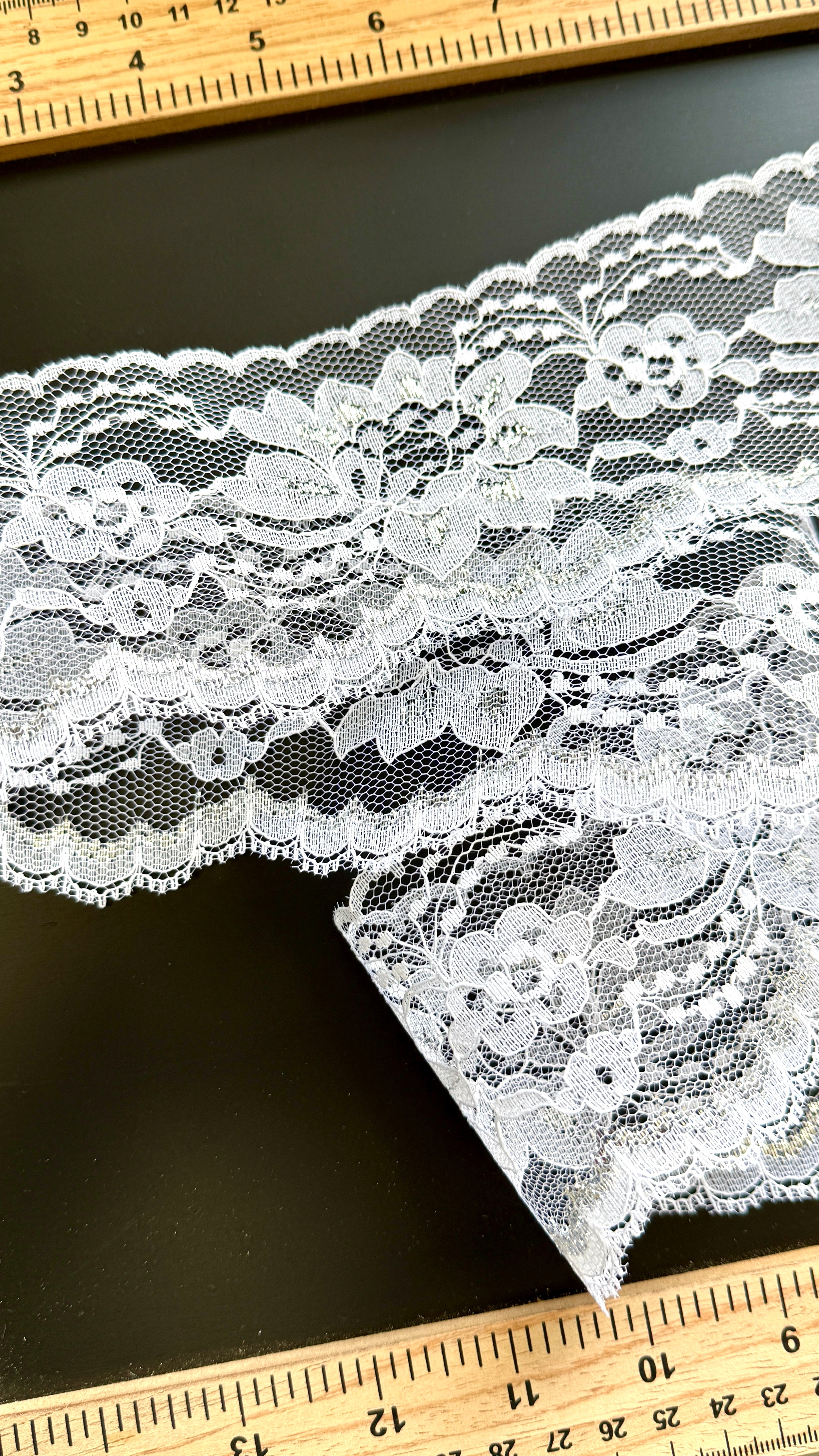 White lace fabric with a ruler for scale on a black background